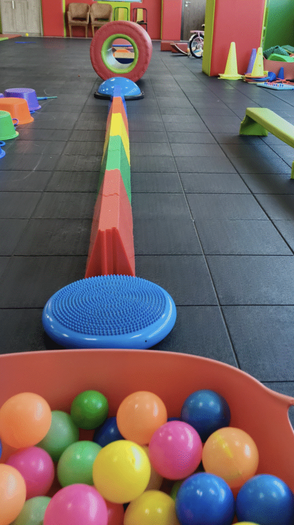 Colorful sensory obstacle course setup with balance beams, therapy balls, and cones for pediatric therapy sessions.